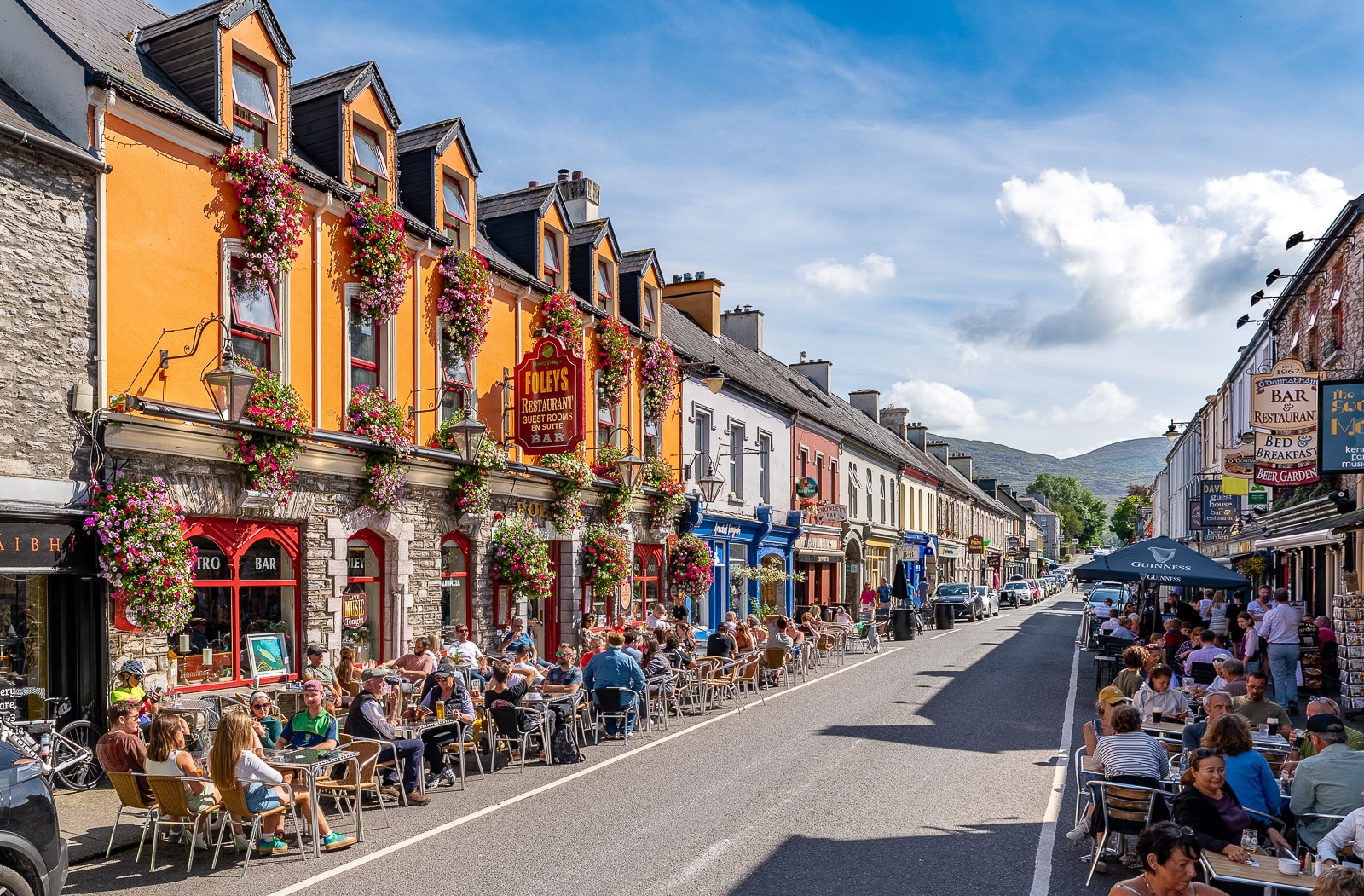 Busy Street in Kenmare with colourful buildings and people dining outdoors on a sunny day.